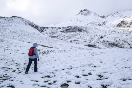 an unrecognizable woman dressed in mountain clothes and a small red backpack, crosses a snowy mountain passage on a winter hikeの写真素材