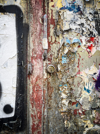 Close up of an old metal door covered in layers of peeling paint, rust, and torn posters, revealing textures, colors, and urban decay in a gritty street sceneの写真素材
