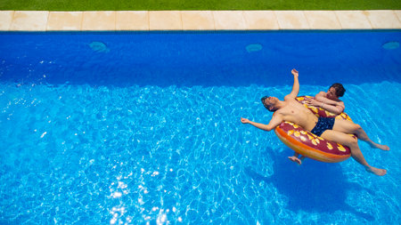 Young couple relaxing on a pastry ring pool float in clear blue water on a sunny day, the girl...