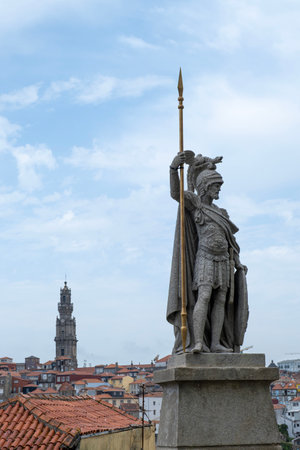 Statue of a roman warrior or centurion with spear overlooking the rooftops of Porto, with the iconic Clerigos Tower rising in the background under a bright blue skyの写真素材