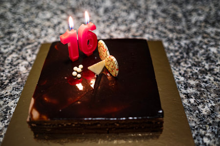 close-up of a delicious dark chocolate birthday cake with a candle celebrating 16 years, decorated...