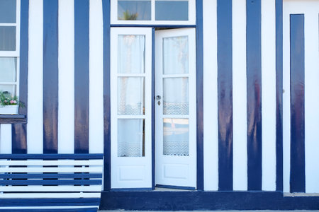 a blue and white striped house facade with a wooden bench and a open door, decorated with flower pots, Costa Nova, Aveiro, Portugalの写真素材