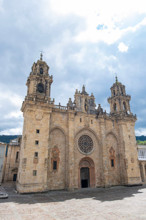 Historic stone cathedral of Mondonedo, Galicia, Spain, with ornate towers and a large rose window under dramatic clouds in a quiet plaza,の写真素材