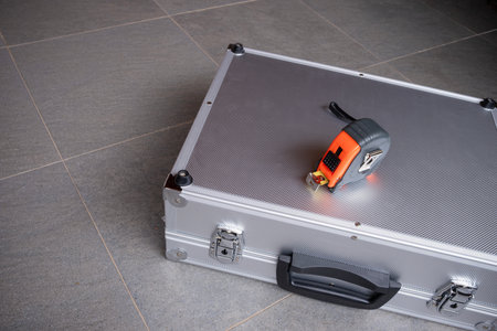 A tape measure rests on a metallic tool briefcase set on a gray tiled floor, construction, home improvement, professional tools, and precision with ample copy spaceの写真素材