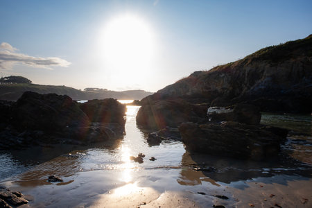 Sunset light reflecting on wet sand and rocks at a peaceful coastal inlet, creating a serene and dramatic seaside landscapeの写真素材