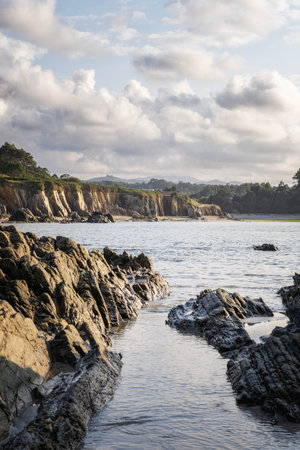 Rocky coastal landscape at low tide, with textured cliffs and calm water under a sky filled with soft evening clouds, Porcia beach, Asturias, Spainの写真素材