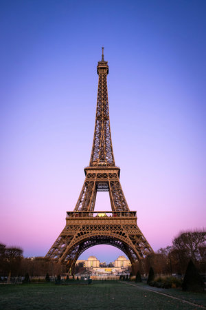 Vertical view of the Eiffel Tower at sunset with a pink and purple gradient sky. Iconic Parisian...