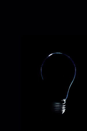 Minimalist silhouette of a light bulb against a black background with subtle blue rim lighting....
