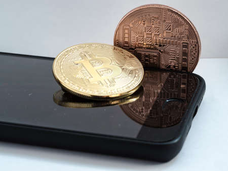 Two metal bitcoins on top of mobile, with white background.の写真素材