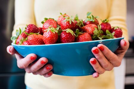 Woman holding blue bowl with red strawberries and yellow backgroundの写真素材