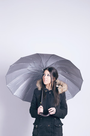 Happy woman wearing a coat, holding an umbrella, over gray backgroundの写真素材