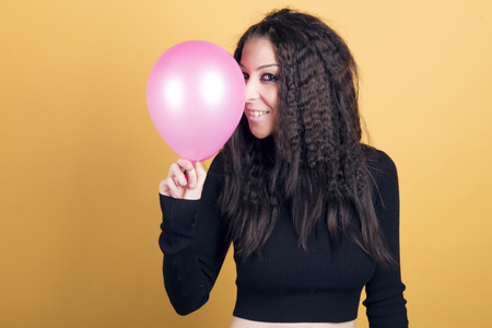 Happy woman playing with a pink balloon over a yellow background.の写真素材