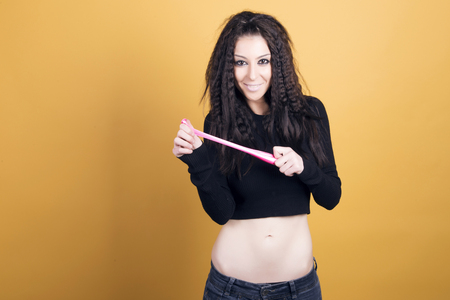 Happy woman stretching a pink balloon over a yellow background.の写真素材