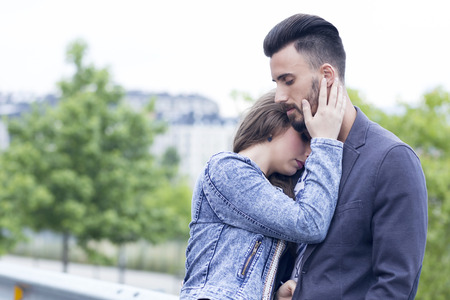 Young couple in love outdoors, in the city near a group of trees. She is touching his face, very close to him.の写真素材