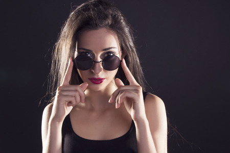 Cool swag girl in a black tank top, looking over her sunglasses, over a black background.の写真素材