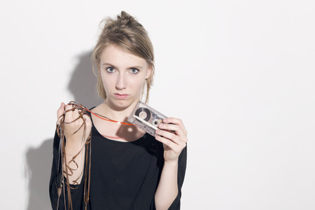 Young blonde woman damaging a cassette tape, looking to camera, over a white background.の写真素材