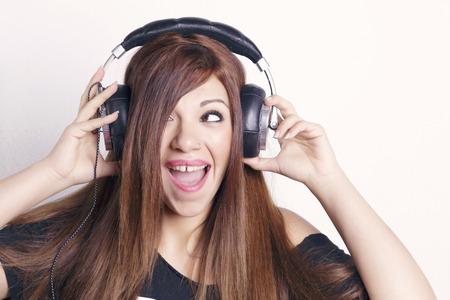 Brunette woman with headphones and a black t shirt having fun, over a white wall.の写真素材