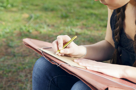 Young brunette woman artist, drawing sketch and thinking, looking for inspiration. Outdoors, in nature.の写真素材