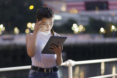 Girl using a tablet pc, outdoors, at night in the city. Shallow depth of focus, focus on her eyes.の写真素材