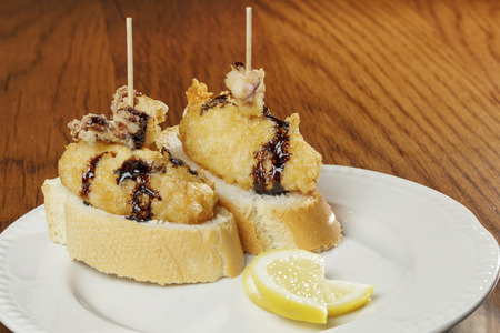 Classic spanish tapas: two fried calamari served with bread on a dish. Spanish name Chipirones.の写真素材