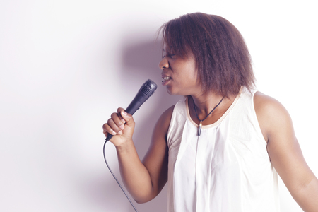 Young african woman singing holding a microphone, cheerful and funny, indoors, over a white background.の写真素材