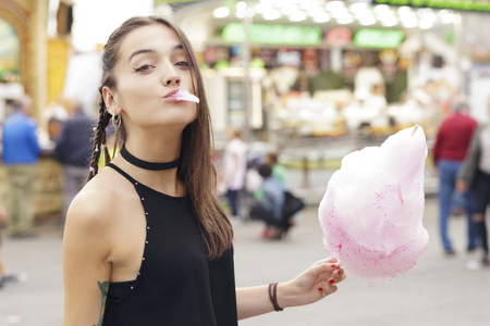 Pretty brunette girl eating cotton candy at fairground.の写真素材