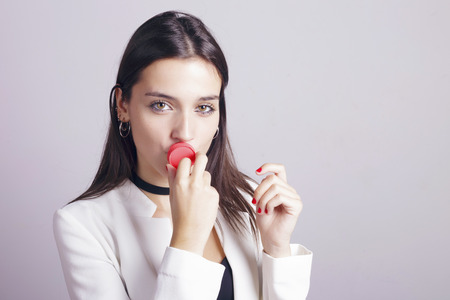 Brunette girl applying lip balm moisturizing balm, kissing directly the jar. Over a grey background.の写真素材