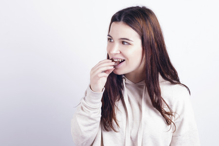 Young brunette girl eating a chocolate palm, a typical spanish bun. Indoors, over a grey wall.の写真素材