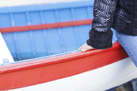 Young woman sitting on an old rowing boat, with her hand touching its wood.の写真素材