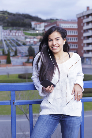 Young latin woman listening to music on the street, on a cloudy afternoon.の写真素材