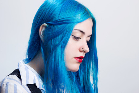 Portrait of a young woman with blue hair, indoors, in a white wall background.の写真素材