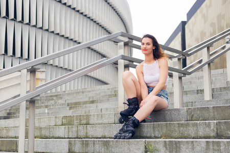 Roller girl resting, sitting on a stairs in the city. On a cloudy day.