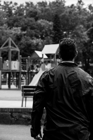 Worried man looking to a empty city playground. Converted to black and white, grain added.の写真素材