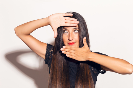 Young adult woman framing her face with her hands, making funny faces. In studio over a white background.の写真素材
