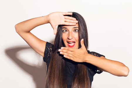 Young adult woman framing her face with her hands, making funny faces. In studio over a white background.の写真素材