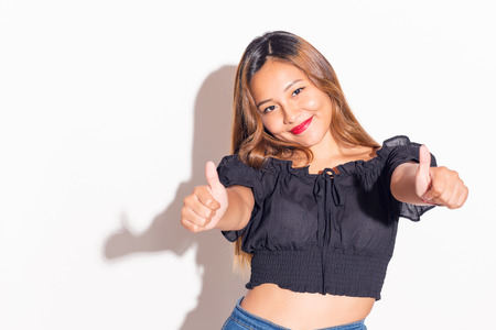 Cheerful latin girl with her thumbs up. Indoors, over a white wall.の写真素材