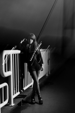 Girl at night on the street, resting on a railing. Converted to black and white, camera shake technique.の写真素材
