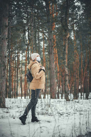 A young girl in winter clothes and in a medical mask walks in the winter forest.の写真素材