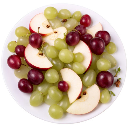 This image showcases a fresh and colorful fruit salad. It includes green grapes, red grapes, and apple slices arranged artistically on a white plate.の素材