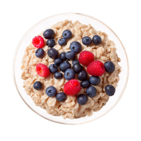 A topdown studio shot shows a bowl of oatmeal topped with several plump blueberries and bright red raspberries on a white background. Healthy food.の素材