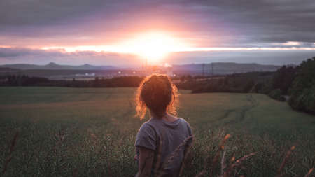 Young woman standing on a wheat field with sunrise on the backgroundの写真素材