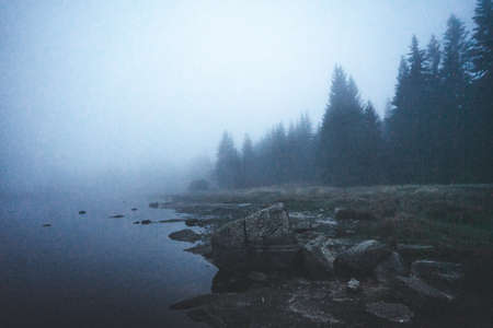 Coastal landscape of foggy lake. Stones in the water on foreground. Long exposure shot.の写真素材