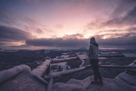 Woman leaning on the railing and watching how sun is going down. Dramatic wintry scene. Jetrichovice, Czech Republicの写真素材