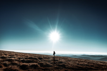 Woman stands on horizon hills with big shinning sun above her head, Krkonose, Czech republic, minimalistic nature scene, blue beautiful skiesの写真素材