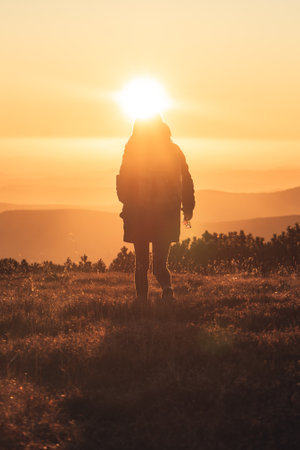 Woman standing on a mountain peak when the sun is going down, beautiful sunset in Krkonose, Czech...