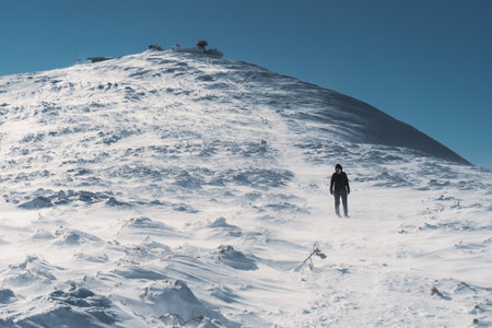 A lone hiker in the cold winter walks on the mountain, on sunny day, clear blue sky, strong wind, Czech republic, Giant Mountainsの写真素材