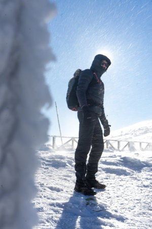 A lone hiker in warm clothes, in the cold winter walks on the frozen mountain, on sunny day with clear blue sky and strong windの写真素材