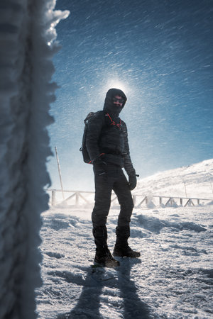 A lone hiker in warm clothes, in the cold winter walks on the frozen mountain, on sunny day with clear blue sky and strong windの写真素材