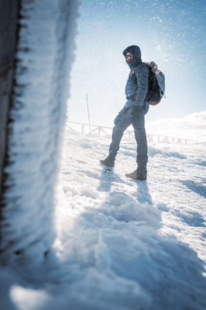 A lone hiker in warm clothes, in the cold winter walks on the frozen mountain, on sunny day with clear blue sky and strong windの写真素材