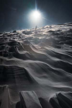 A lone hiker in warm clothes, in the cold winter walks on the frozen mountain, on sunny day with clear blue sky and strong windの写真素材